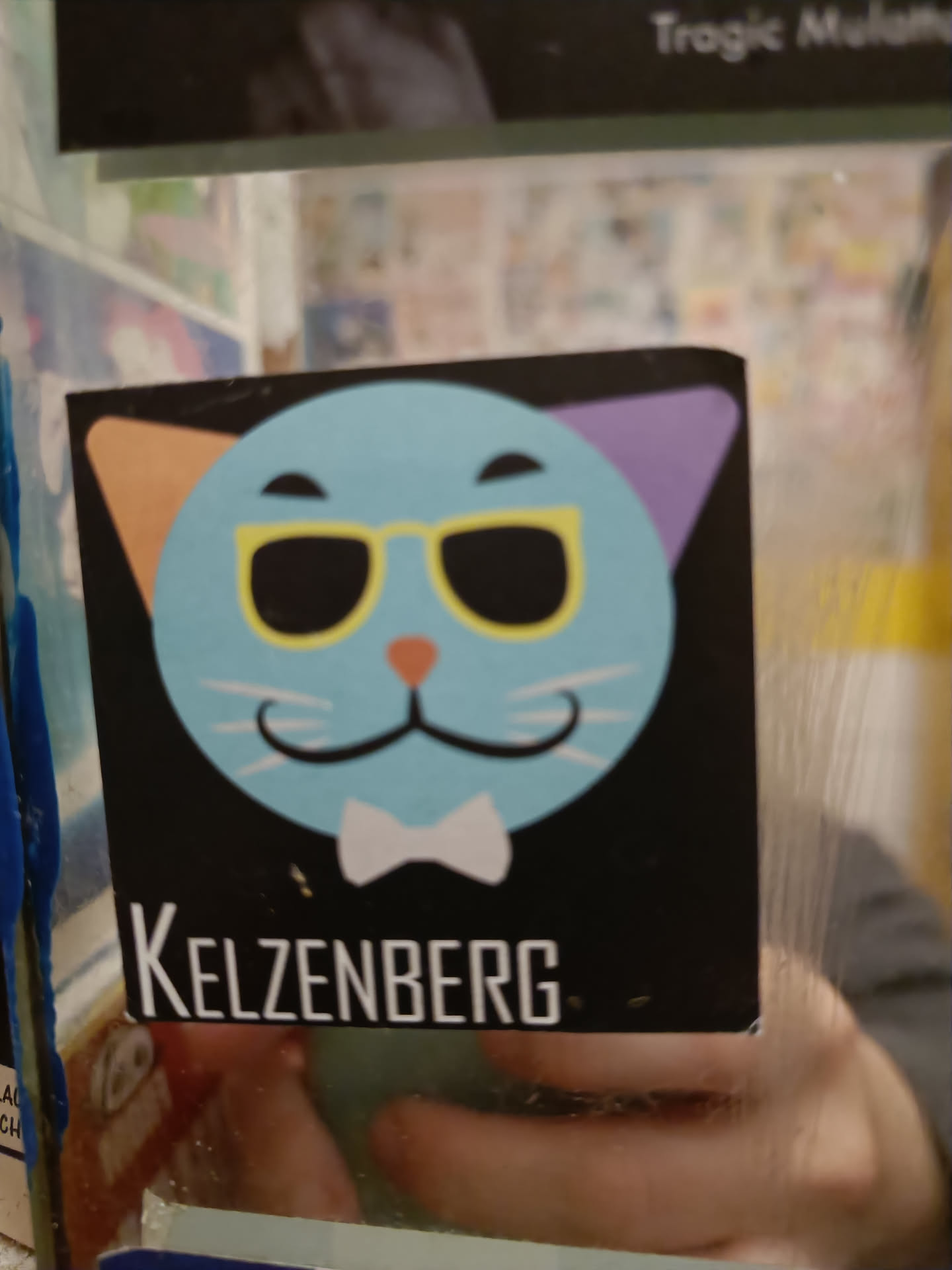 A sticker featuring a cartoon cat wearing sunglasses and a bow tie. The cat's ears are different colors. The text "Kelzenberg" is at the bottom of the sticker.