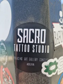 Black and white sticker for Sacro Tattoo Studio in Adelfia, advertising their services: piercing, art gallery, and concept. The sticker has a round shape and features the studio's name and services in a minimalist design.