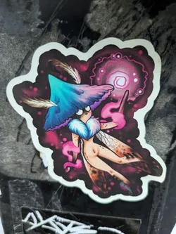 A vibrant sticker featuring a whimsical fairy with mushroom-like features, casting a spell with a glowing orb. The art style is dark fantasy with splashes of pink and purple.