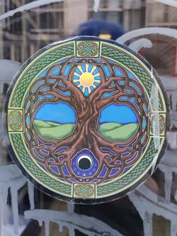 Round sticker featuring a detailed illustration of the Tree of Life surrounded by Celtic knotwork. The artwork includes a sun and moon, symbolizing day and night or balance. The colors are vibrant, and the design is intricate.