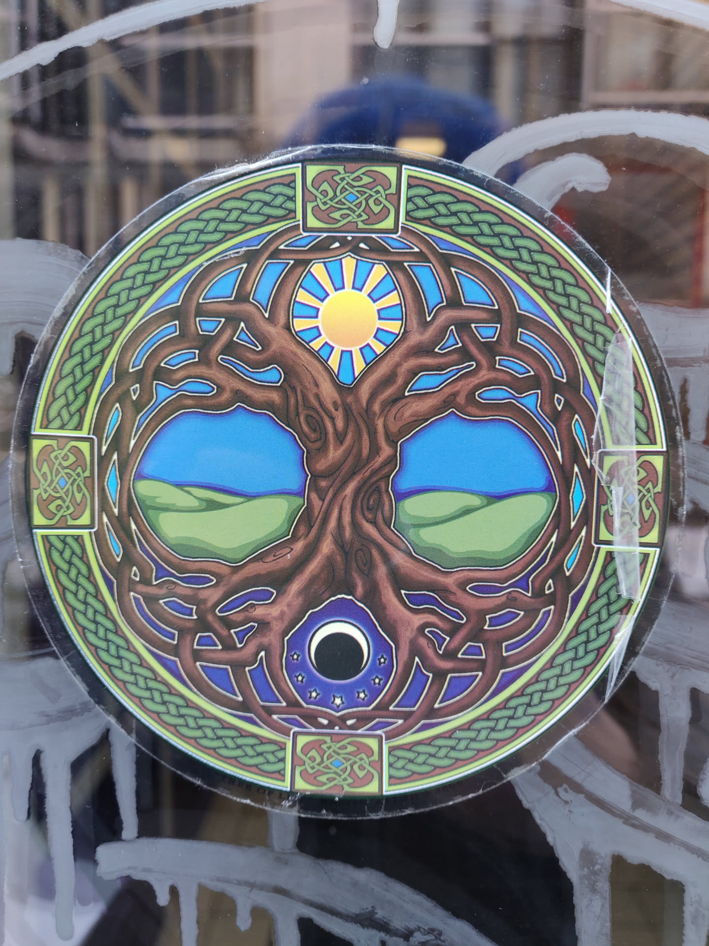 Round sticker featuring a detailed illustration of the Tree of Life surrounded by Celtic knotwork. The artwork includes a sun and moon, symbolizing day and night or balance. The colors are vibrant, and the design is intricate.