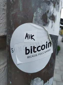 A round white sticker with black text that says Bitcoin Because Fuck Banks. There is a smaller white square sticker on top that says AIK.