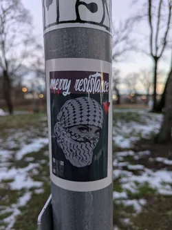 Sticker featuring a woman wearing a keffiyeh, with the text "Merry Resistance".  The style is graphic and impactful.