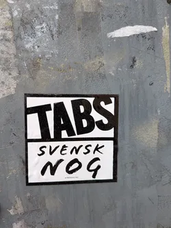 A rectangular black and white sticker featuring bold typography. The sticker is divided into two horizontal sections by a thin black line. The top section displays the word 'TABS' in large, thick, slightly tilted black capital letters against a white background. The bottom section, also on a white background, features the word 'SVENSK' in a smaller, brushstroke-style black font, followed by 'NOG' in a larger, more prominent brushstroke-style black font. A thin black border frames the entire sticker. At the very bottom, in small black text, it reads 'STREAMA NU'. The sticker is affixed to a textured, weathered grey surface.