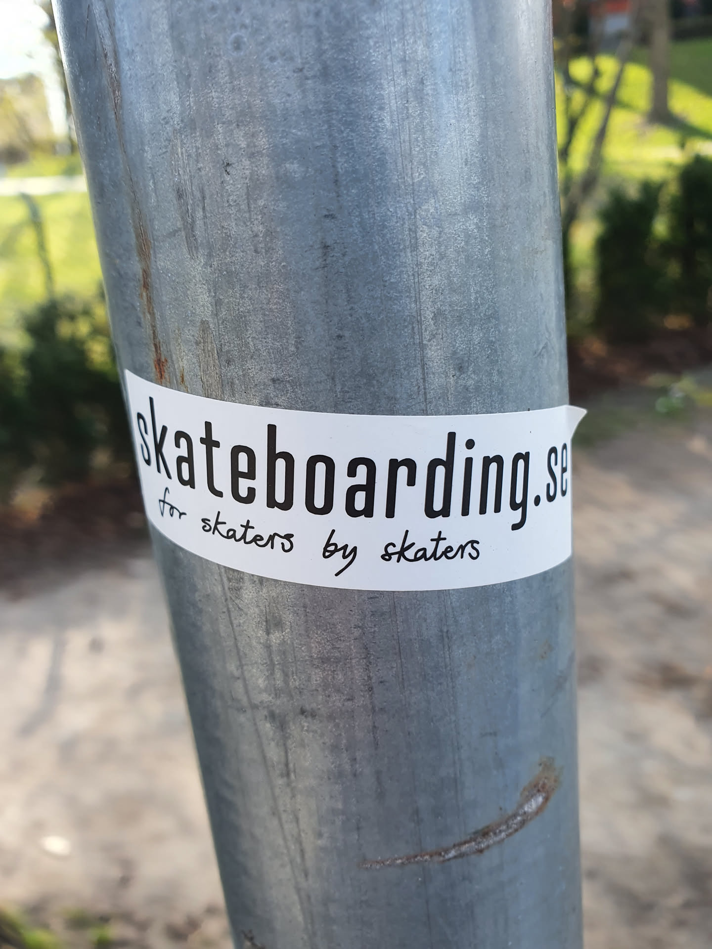 A white sticker on a metal pole. The sticker features the text "skateboarding.se" in a bold font, with the smaller text "for skaters by skaters" written below it.