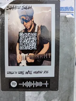 The sticker features a stylized image of Sammer Salah playing a guitar, framed as if it were a Polaroid photo. Above the guitarist is the name "Sammer Salah". A QR code is superimposed on the center of the image. Text below the image reads "ROCK'N ROLL WILL NEVER DIE". A Spotify code completes the sticker at the bottom.