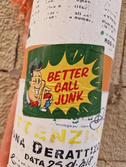 A vintage-style sticker featuring a cartoon character and the text "Better Call Junk". The sticker has a green and yellow color scheme. It's been affixed to what appears to be a cylindrical object. 