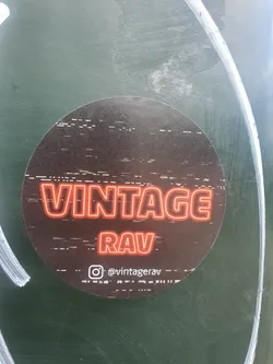 Round sticker with a dark background and glitch effect.  The text "VINTAGE RAV" is displayed in neon red. An Instagram handle is visible at the bottom.