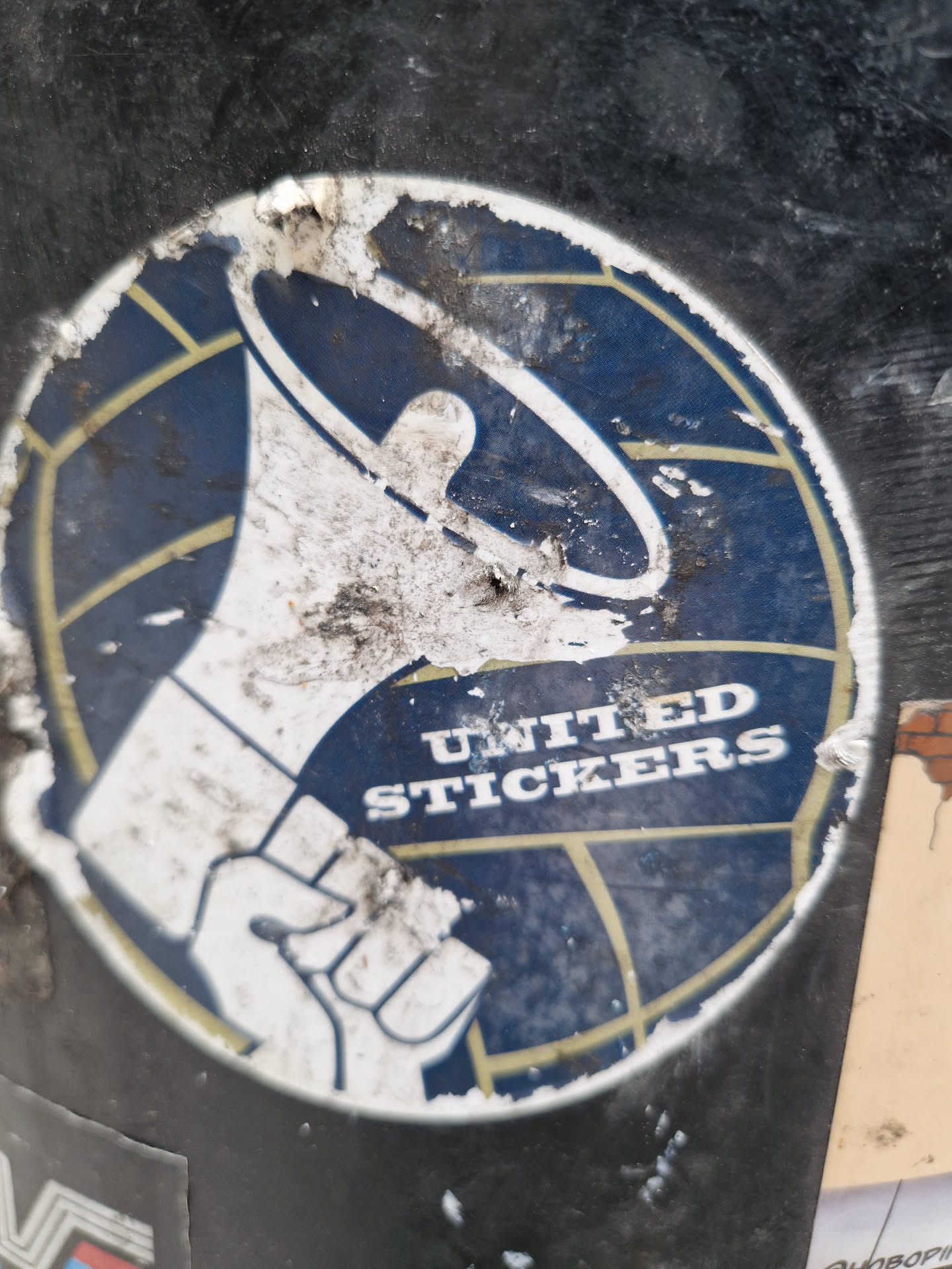 This sticker shows a graphic of a clenched fist holding a megaphone in front of a stylized world map.  The text "UNITED STICKERS" is prominently displayed. The sticker appears to be old and worn, with significant dirt and damage visible.