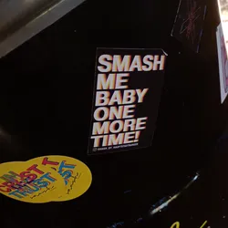A black sticker with colorful text. The text says "Smash me baby one more time!" in a retro style. There is a small Instagram handle at the bottom.