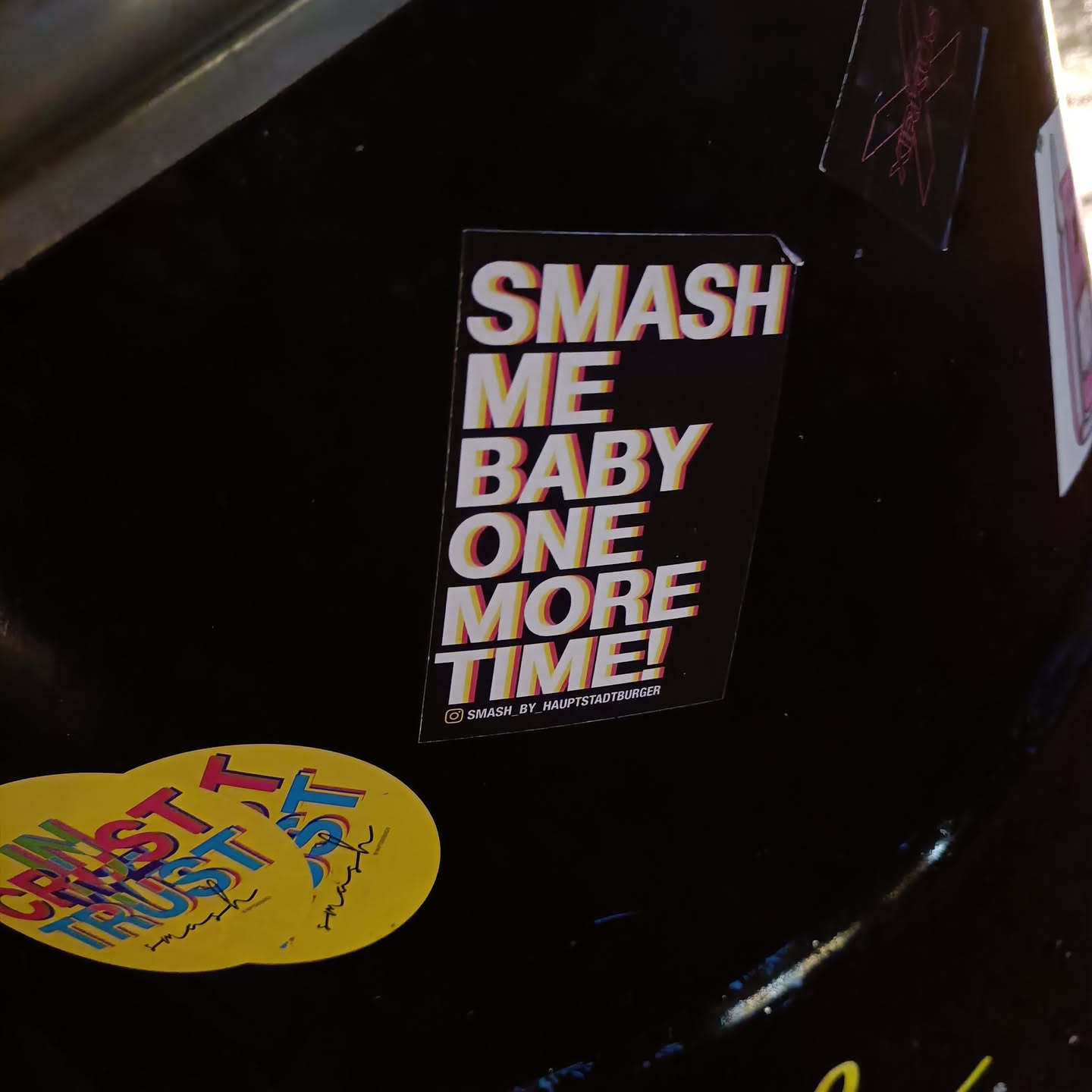 A black sticker with colorful text. The text says "Smash me baby one more time!" in a retro style. There is a small Instagram handle at the bottom.