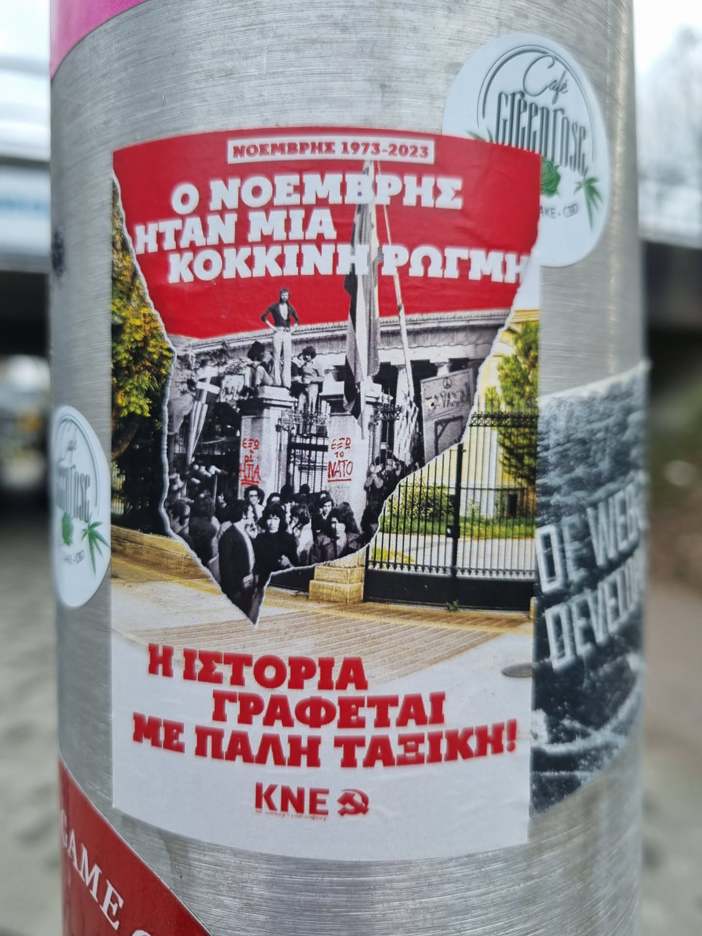 A sticker commemorating the November 1973 uprising in Greece. The sticker features a collage of images from the event and text in Greek.  The text translates roughly to: 'November 1973-2023. November was a red crack. History is written with class struggle!'  The abbreviation KNE is visible, likely referring to a political organization.