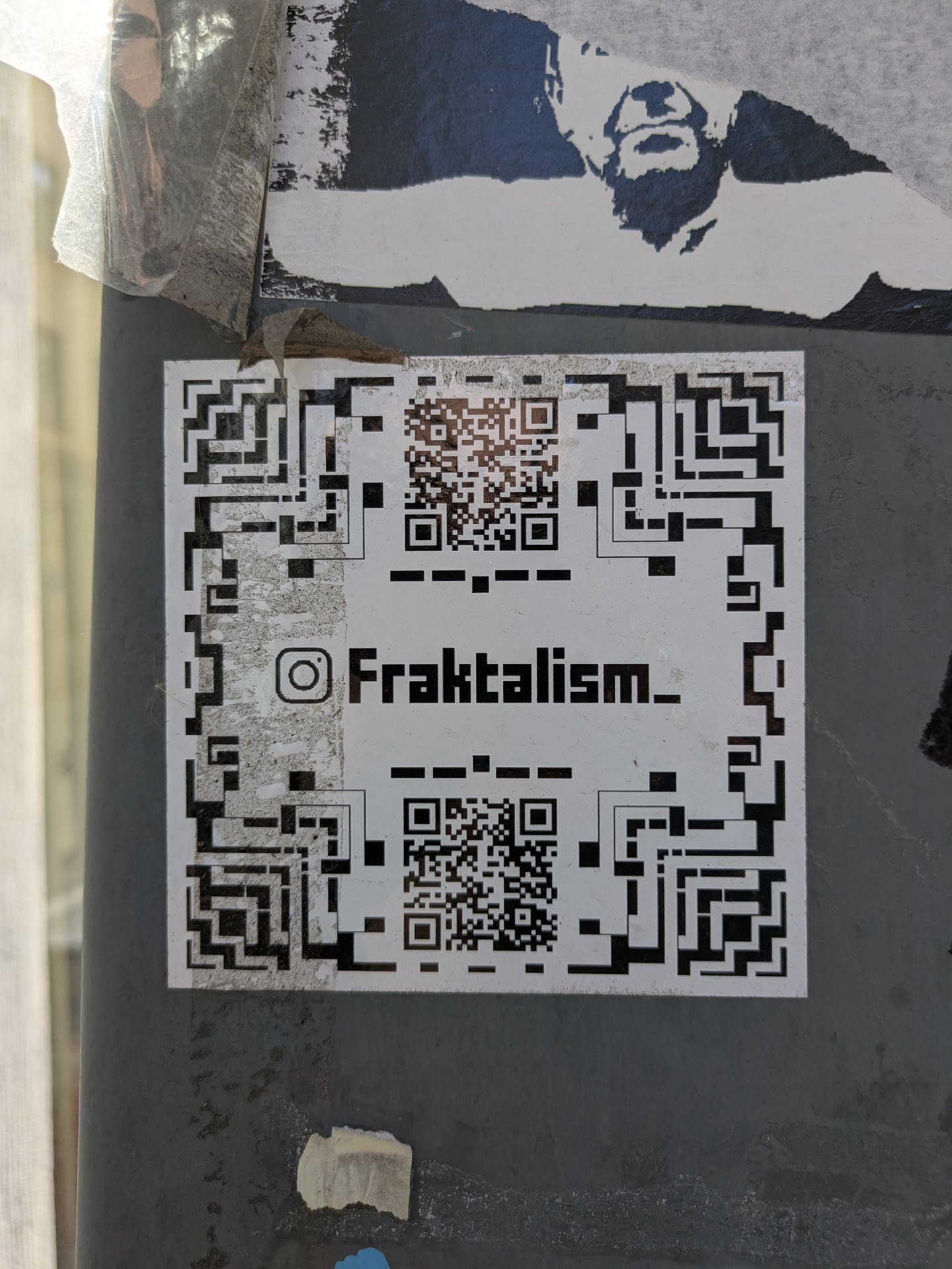 This is a sticker featuring a complex design primarily consisting of QR code patterns around the edges and center. An Instagram handle, @Fraktalism_, is printed prominently in the middle. This sticker likely serves as a creative way to direct people to an online presence using a scannable QR code.