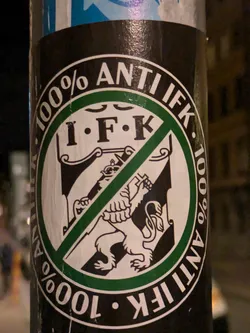 A round sticker with a lion emblem crossed out. The text "100% ANTI IFK" is written around the circle. 