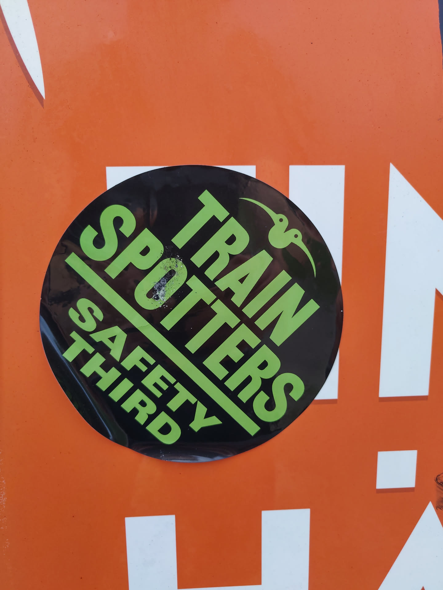 A round black sticker with the text "Train Spotters" in green and "Safety Third" in white. There is a small drawing of two birds in the upper right corner.