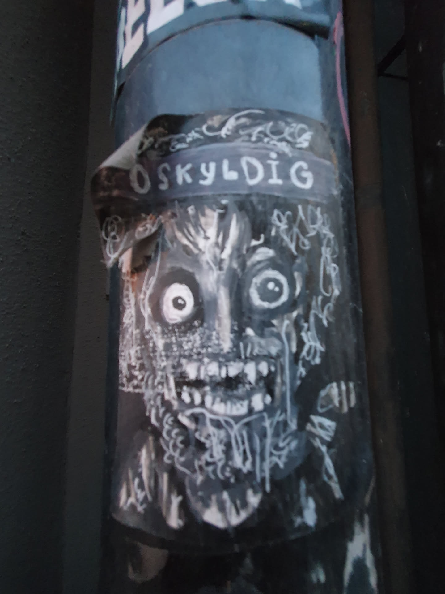 Black and white sticker featuring a frightening creature with large eyes and sharp teeth. The word "OSKYLDIG" is visible at the top of the sticker. The artwork style is reminiscent of horror or dark fantasy illustrations.