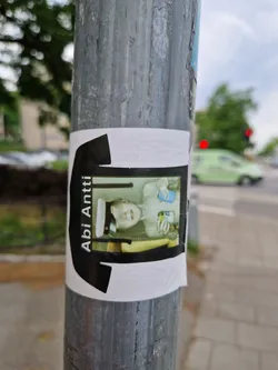 A sticker featuring a photo of a person in a sailor hat holding two drinks. The photo is set against a black t-shirt design.