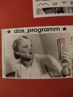 Black and white photo of a woman looking at herself in a mirror, wearing a mask. The sticker features the band's name and Bandcamp link. 