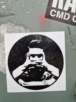 A monochrome round sticker featuring a stylized illustration of a person wearing sunglasses and appearing to be holding something in front of them. The style is reminiscent of stencil art or a screen print.  The image is predominantly black and white, with strong contrasts.
