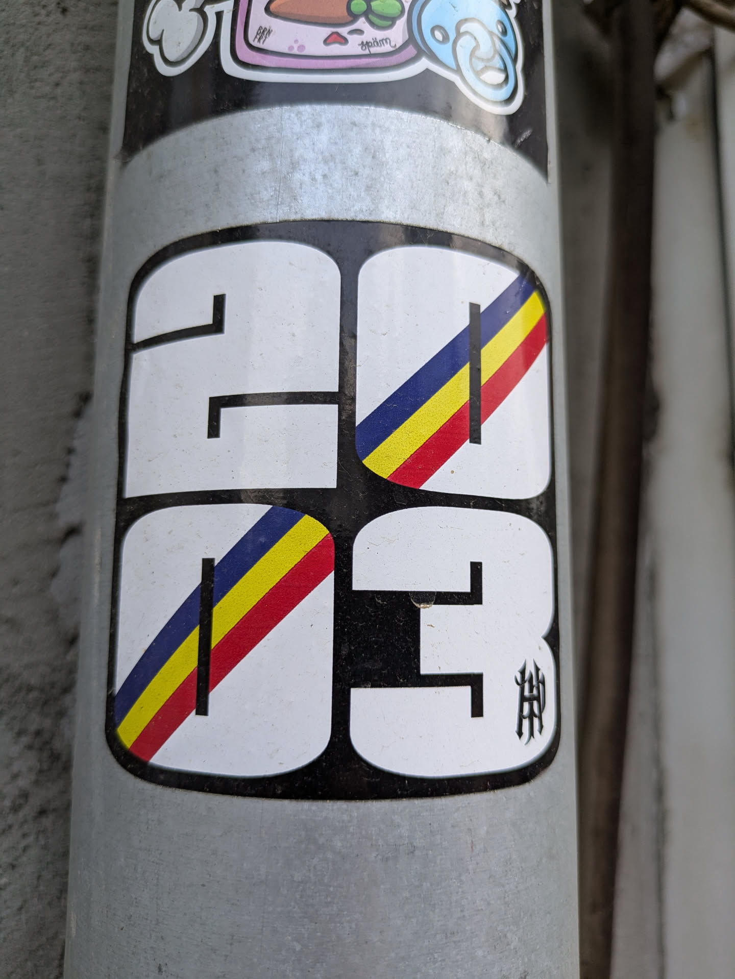 The sticker features the year "2023" with a stylized design. Each number is contained within a rounded square. A band of red, yellow and blue spans across all numbers. The last number also contains a stylized symbol on the bottom right corner.