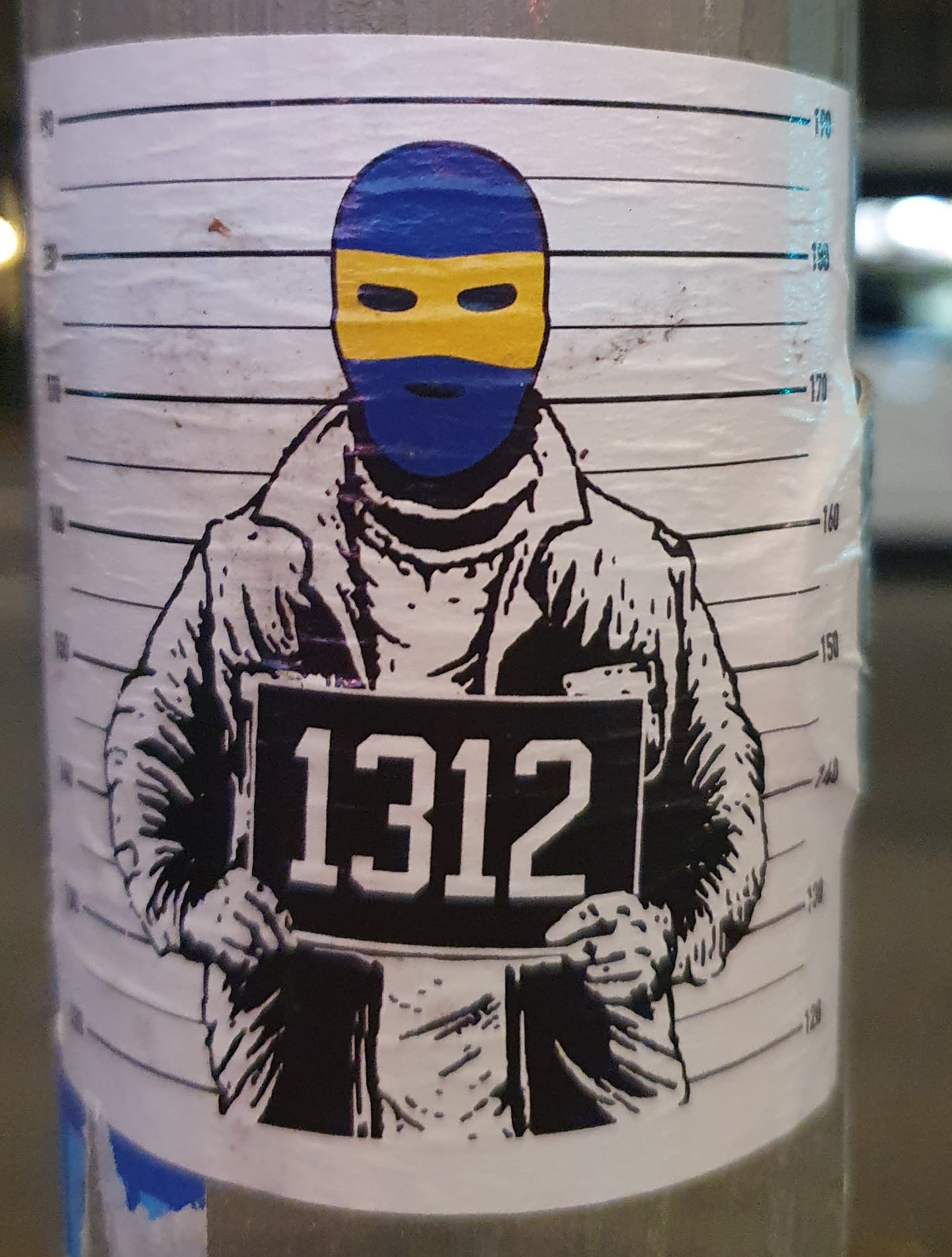 This sticker depicts a person wearing a balaclava with yellow accents, holding a sign that reads "1312." The style is reminiscent of a police mugshot.