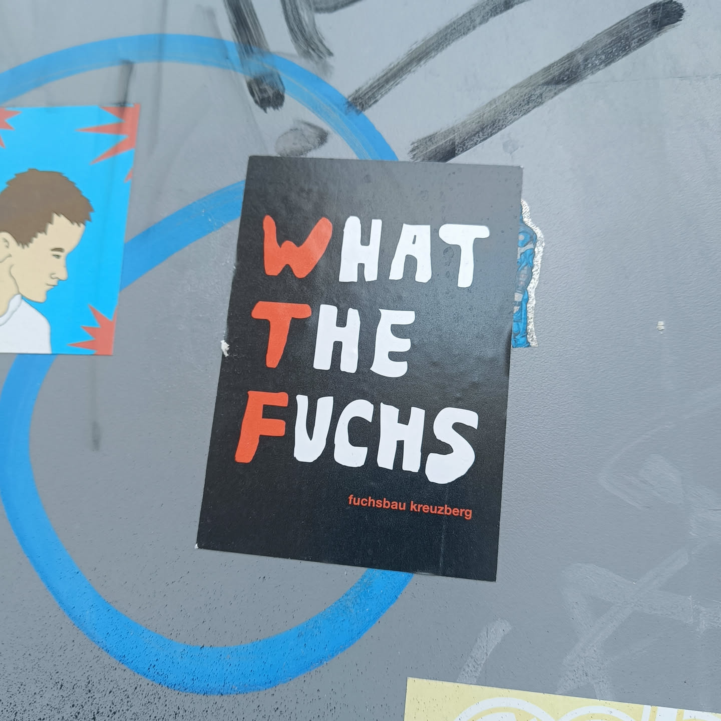 A black sticker with the text "WHAT THE FUCHS" in stylized red and white lettering.  The smaller text at the bottom reads "fuchsbau kreuzberg".