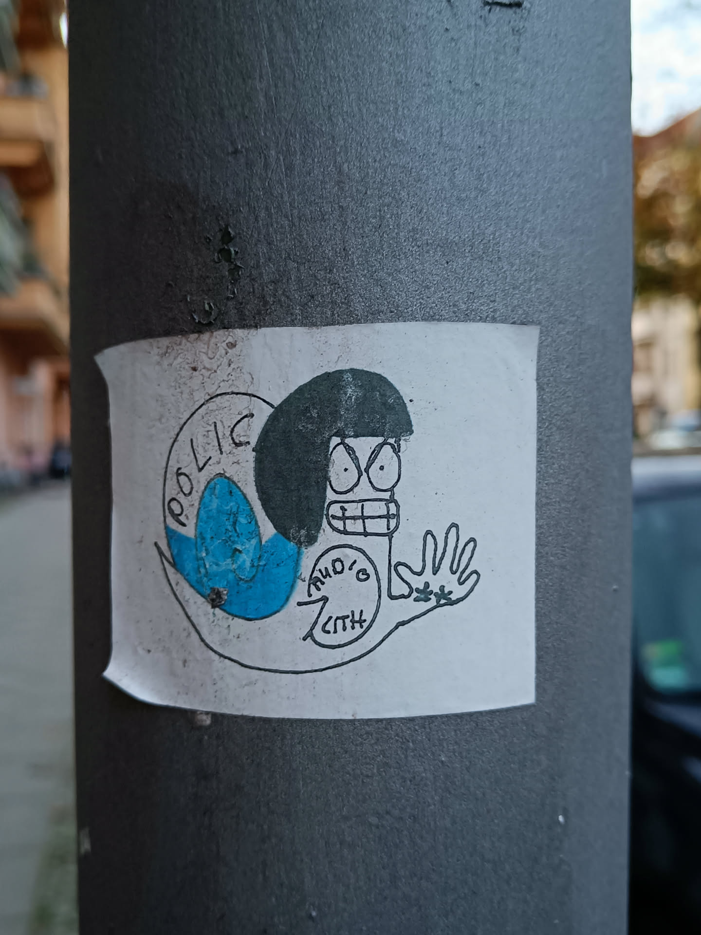 The sticker features a minimalist illustration style, with black outlines and simple coloring. The main character's expression is distinctly annoyed or angry. The sticker appears to be affixed to a gray pole.