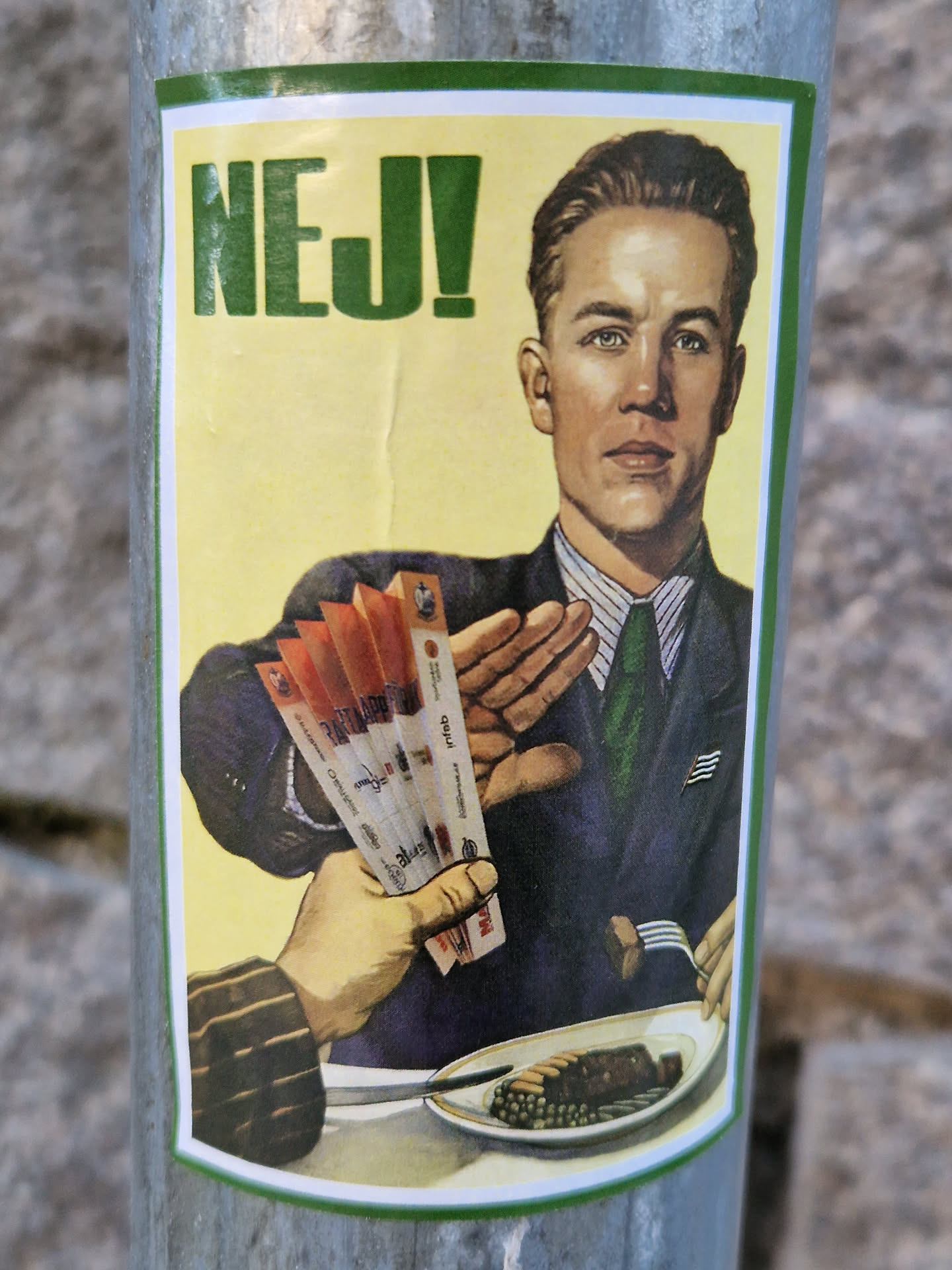 The sticker features an illustration in a retro style. A man in a dark suit with a green tie and a striped shirt is prominently displayed. He has short, neat hair and is making a 'stop' gesture with his right hand, pushing away a hand from the left that is offering him several cigarettes. On the table in front of him, there is a white plate with what appears to be a piece of meat and green peas, and another hand is shown using a fork to take food from the plate. The man also wears a small pin on his lapel that resembles a flag. At the top of the sticker, the word 'NEJ!' is written in large, bold green letters on a yellow background, indicating a refusal or 'No!'. The overall aesthetic suggests a public health or anti-smoking campaign.