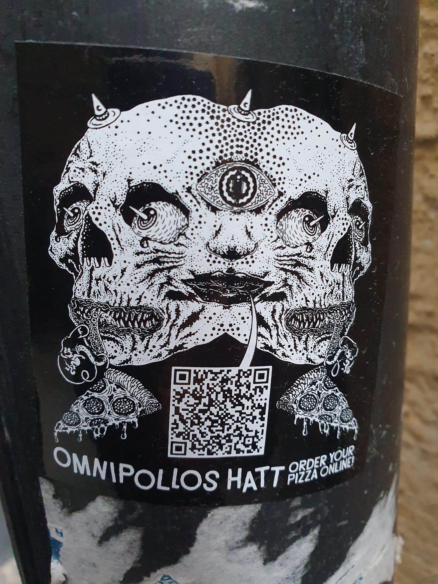 Black and white sticker with a psychedelic illustration of two skulls with a third eye in the middle, holding a pizza slice.  There is a QR code at the bottom with the text 'Order your pizza online!'