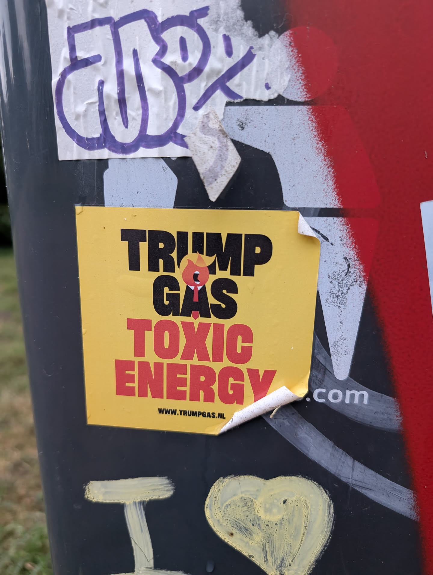 The sticker is rectangular with a bright yellow background. Dominating the center is bold black text reading 'TRUMP GAS' with a small, stylized caricature of Donald Trump, depicted with his signature hair, a red tie, and an open mouth, positioned between 'TRUMP' and 'GAS'. Below this, in large red capital letters, are the words 'TOXIC ENERGY'. At the bottom of the sticker is a website address: 'WWW.TRUMPGAS.NL'. The sticker appears to be slightly creased and peeling at the edges, indicating it has been adhered to a surface.