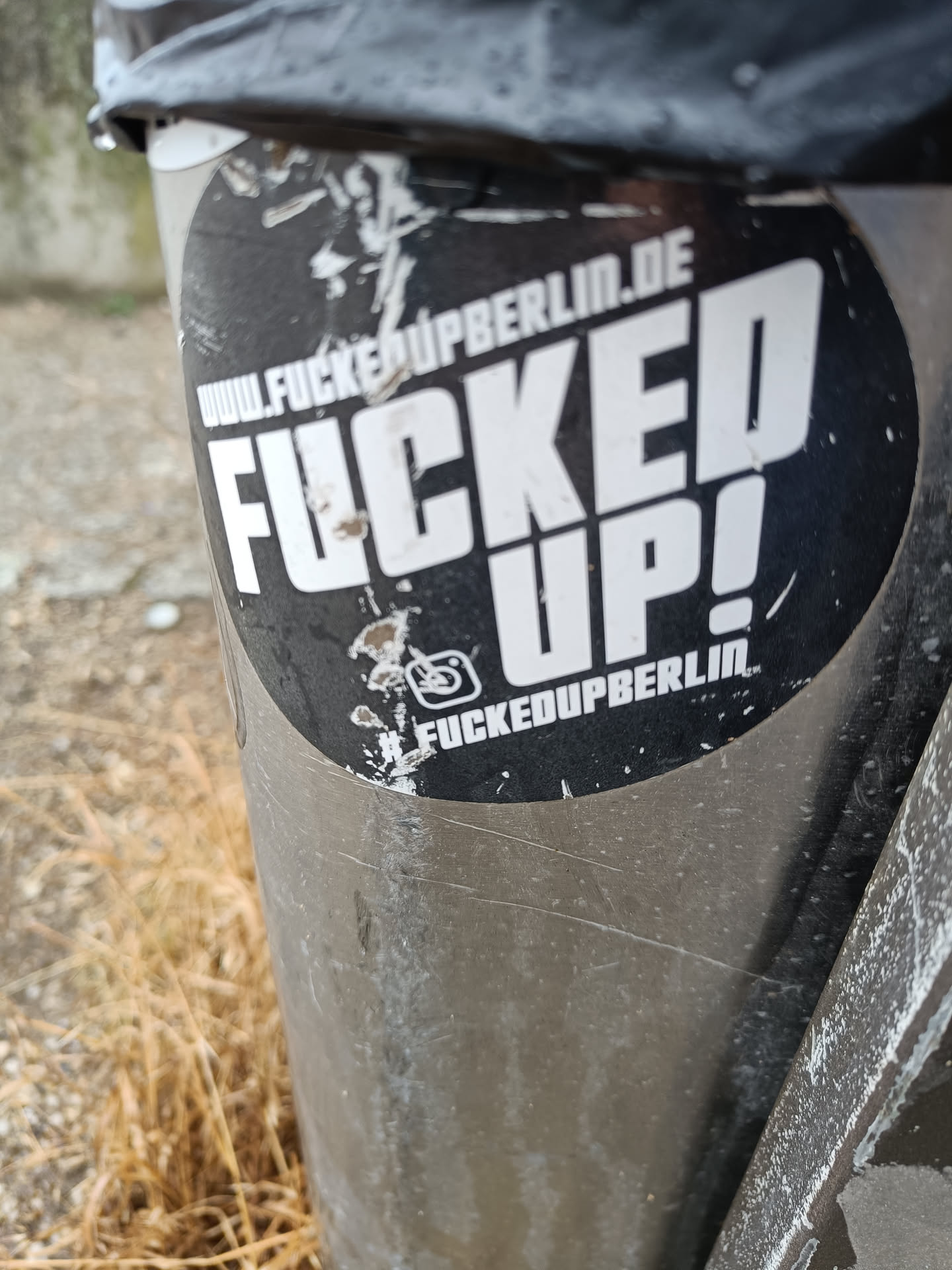 A round black and white sticker with the text "FUCKED UP!" in large letters.  The text "www.fuckedupberlin.de" is visible at the top, and #fuckedupberlin is at the bottom. An Instagram logo is also present. The sticker is affixed to a metal pole.