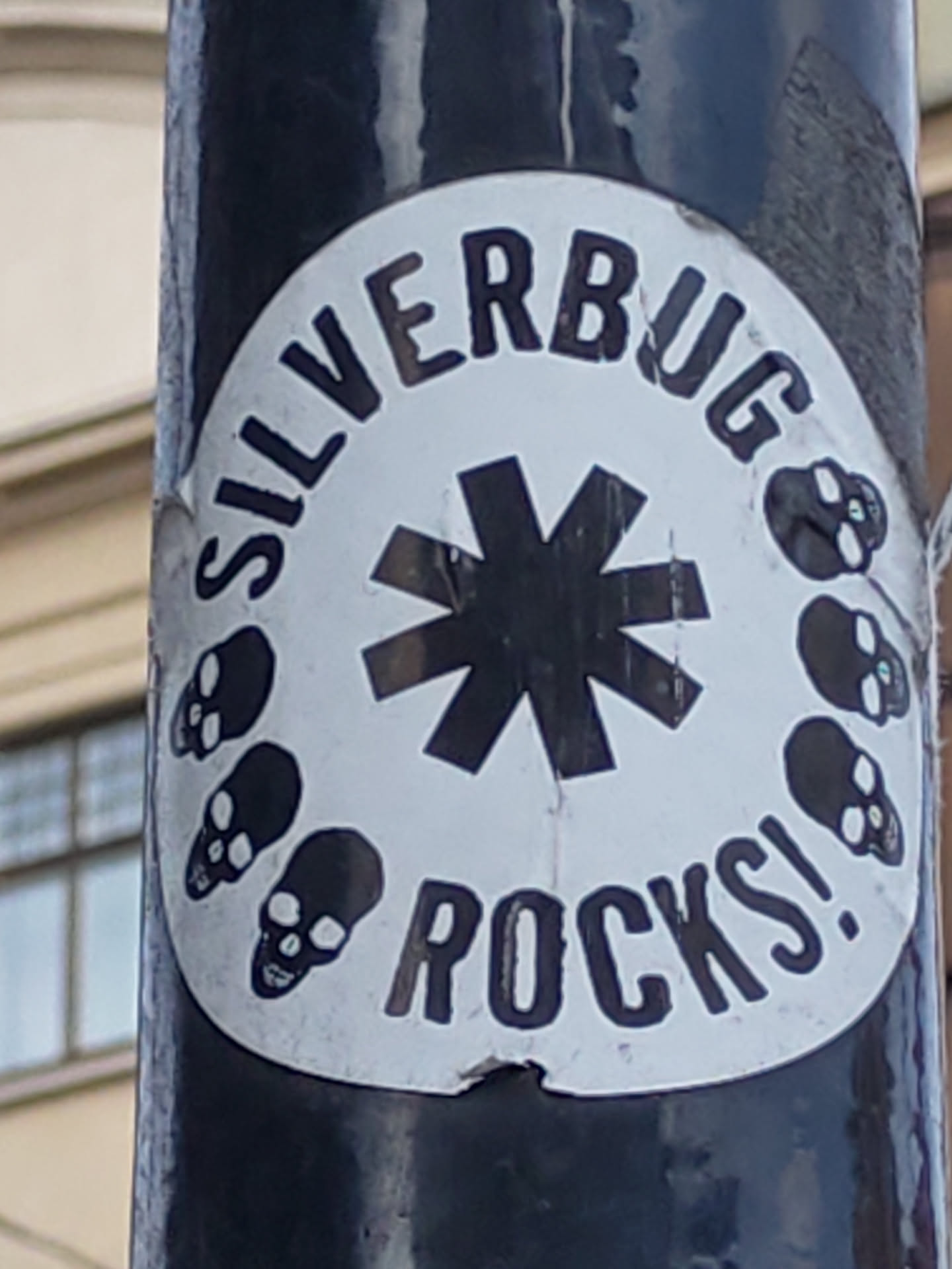 A round sticker with the text "SILVERBUG ROCKS!" arranged circularly around a large asterisk symbol.  There are small skull illustrations around the outer edge of the sticker. The sticker is affixed to a dark-colored pole.