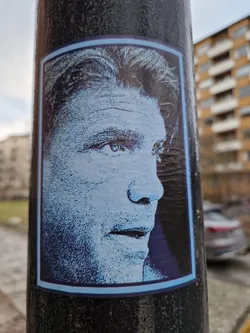 A sticker featuring a profile view of a man's face in blue tones. The style is reminiscent of halftone printing. 