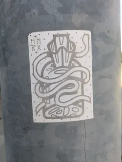 A monochrome sticker adhered to a gray pole features an abstract design. The drawing includes what appears to be a container with swirling elements and organic shapes within it. The letters 'HN' above 'RX', separated by small hearts, are located in the upper-left corner of the sticker.