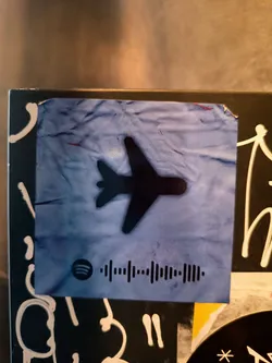 A blue sticker with a plane and a Spotify code.  The Spotify code likely links to a playlist or song related to travel.