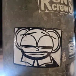 The sticker shows a simplistic cartoon character with a round head, large eyes, and a subtle smile. It's primarily black and white, creating a striking contrast against any background. The character's design is slightly minimalist, giving it a distinctive look.