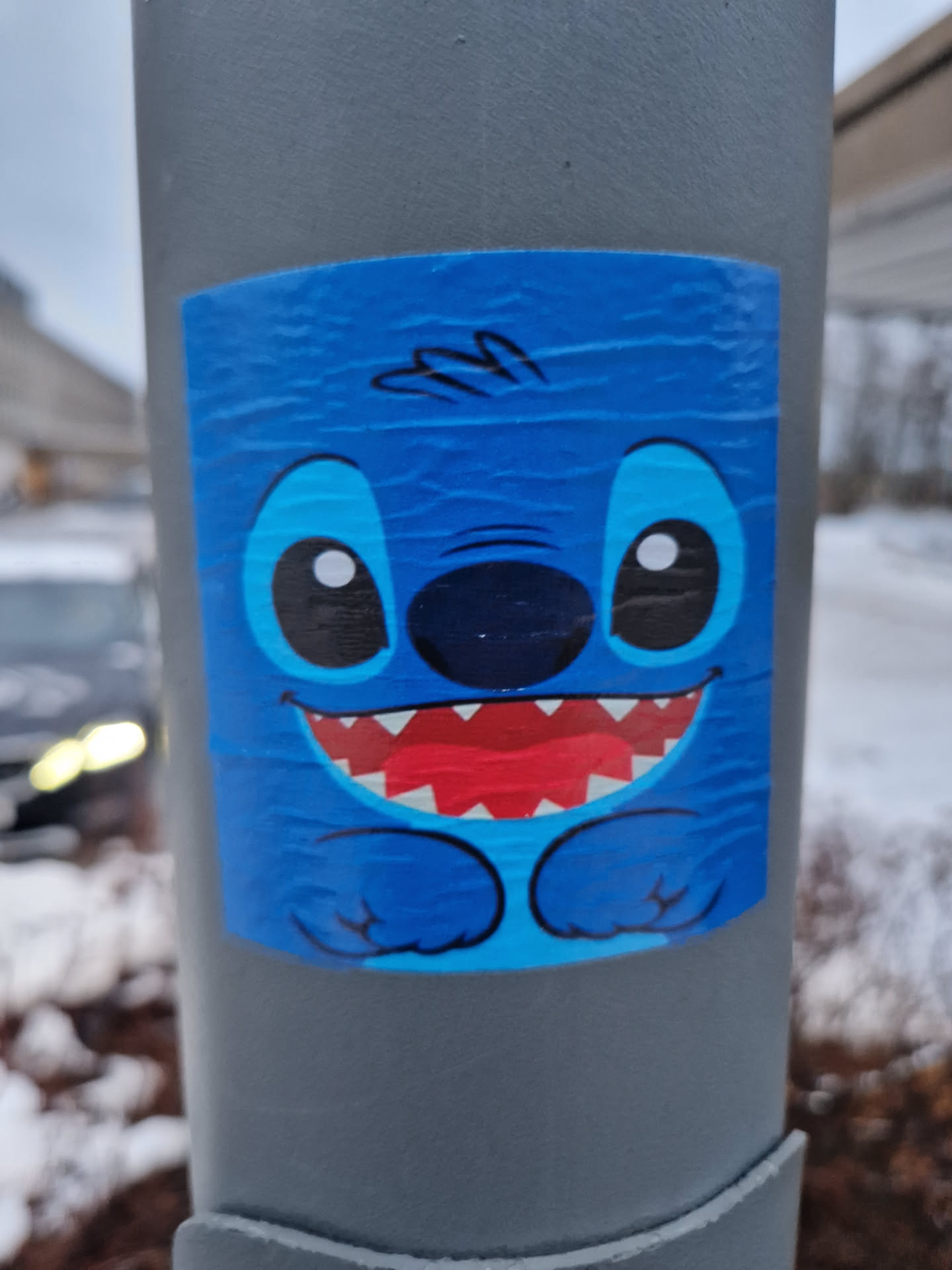 A blue Stitch sticker is applied to a grey pole. The sticker shows Stitch smiling.