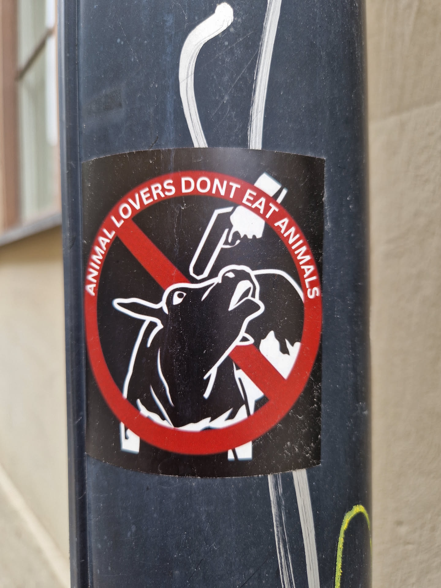 A round sticker with a red circle and a line through it. Inside the circle is a drawing of a cow being slaughtered. The text around the circle says "Animal lovers don't eat animals".