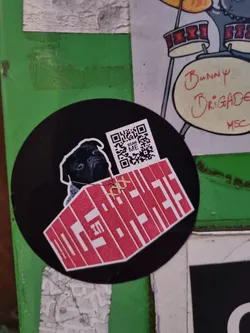Round black and red sticker with a pug wearing a necklace sitting on top of a red coffin-shaped graphic with illegible text inside.  A QR code is present in the top right corner. 