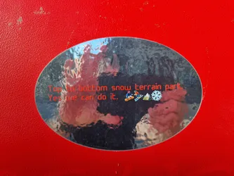 Oval-shaped sticker with a blurry background image and the text 'Top to bottom snow terrain park. Yes we can do it.' in red.  Small icons of skiers and snowboarders are present as well.