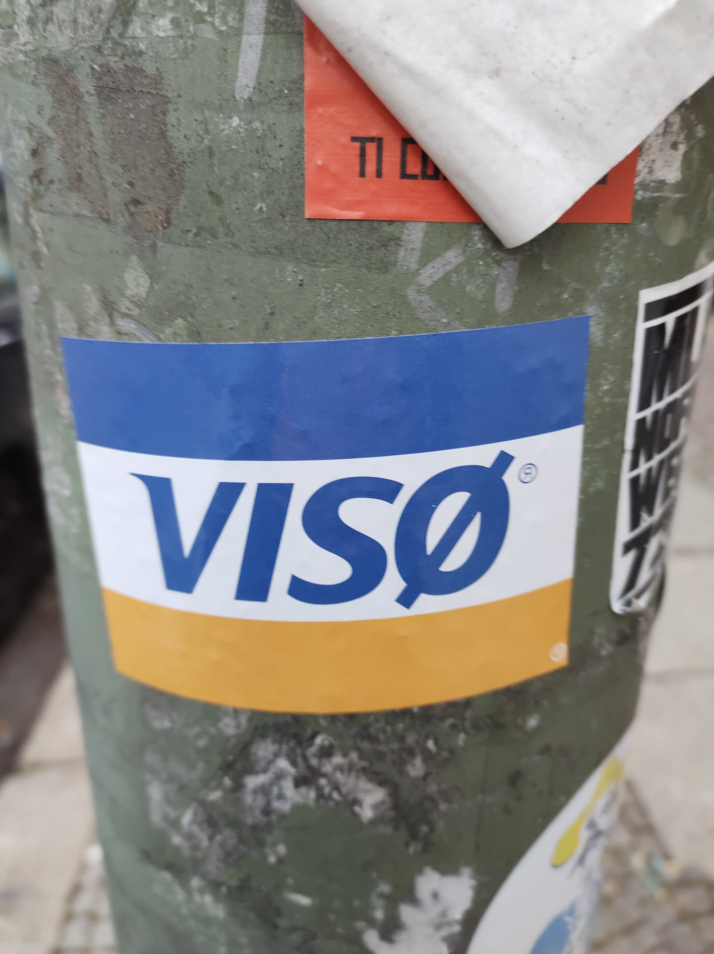 A sticker featuring the Visa logo is affixed to a weathered pole.  The sticker has a blue top section with the Visa logo in white and a yellow bottom section.