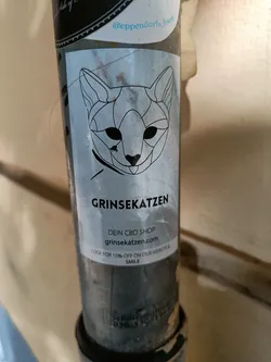 A sticker featuring a geometric cat design and the text "GRINSEKATZEN", "DEIN CBD SHOP", "grinsekatzen.com", and "CODE FOR 15% OFF ON OUR WEBSITE SMILE".