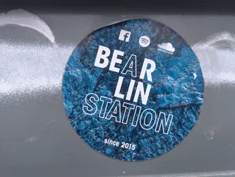 Street sticker Round sticker with a blue and white design. It has the text "BEAR LIN STATION" in bold white letters on a blue background that looks like water or ice. The text "since 2015" is written in smaller white letters at the bottom. The sticker also shows social media icons for Facebook, Spotify, and SoundCloud.