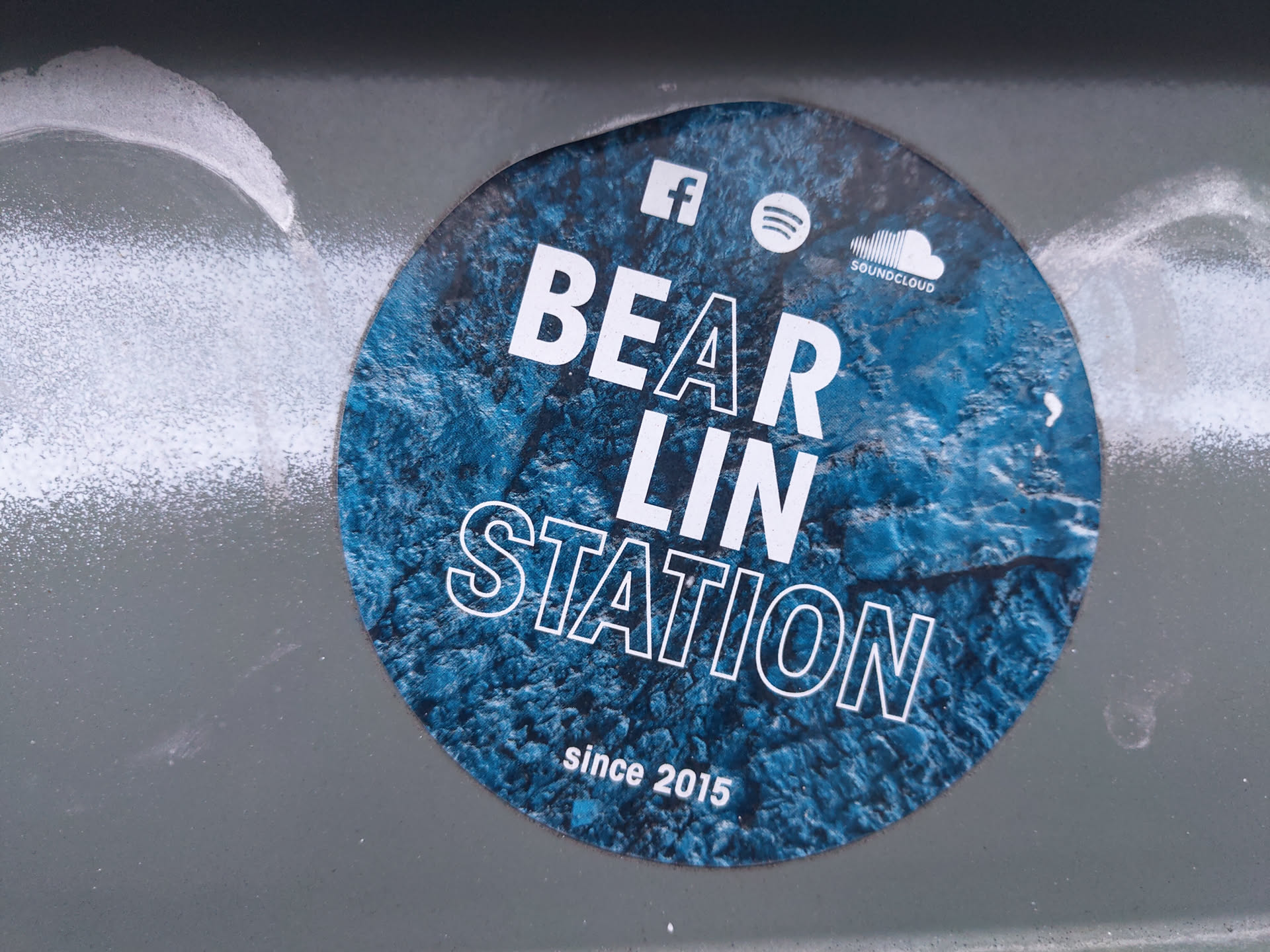 Round sticker with a blue and white design. It has the text "BEAR LIN STATION" in bold white letters on a blue background that looks like water or ice. The text "since 2015" is written in smaller white letters at the bottom. The sticker also shows social media icons for Facebook, Spotify, and SoundCloud.