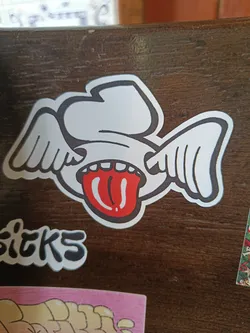 A sticker depicting a cartoonish face with wings and a long tongue sticking out. The style is playful and slightly edgy.