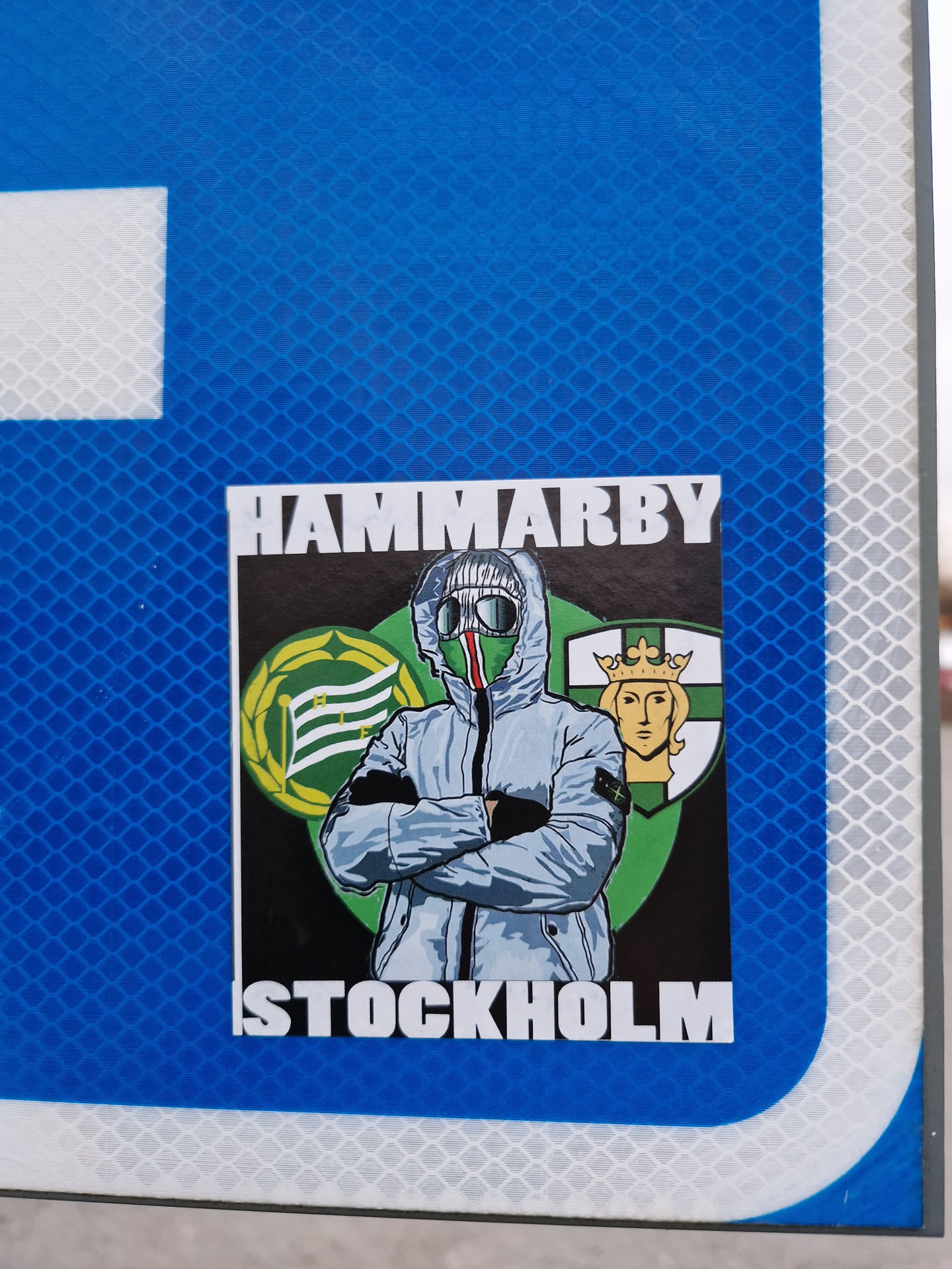 A sticker featuring a stylized illustration of a person wearing a hooded jacket, with the words "HAMMARBY" and "STOCKHOLM" at the top and bottom, respectively.  The image is set against a background that includes a crest or logo.