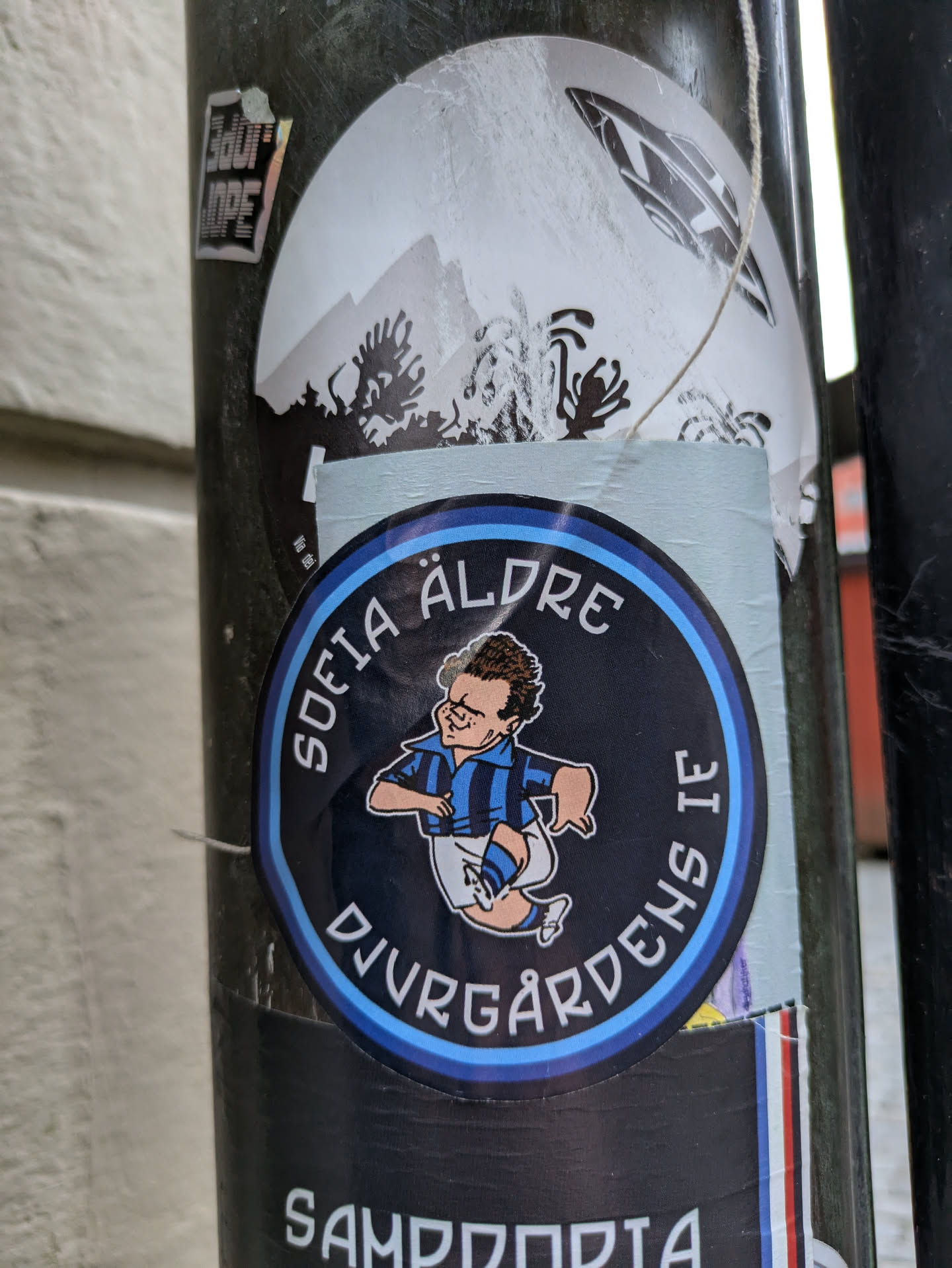 A round sticker featuring a cartoon illustration of a soccer player with the text "Sofia Äldre Djurgårdens IF" around the illustration. The sticker has a black background with light blue accents.