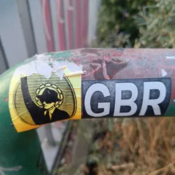 A yellow and black sticker featuring a man in a suit and hat, reminiscent of a secret agent. The text 'GBR' is visible on a separate sticker next to it.