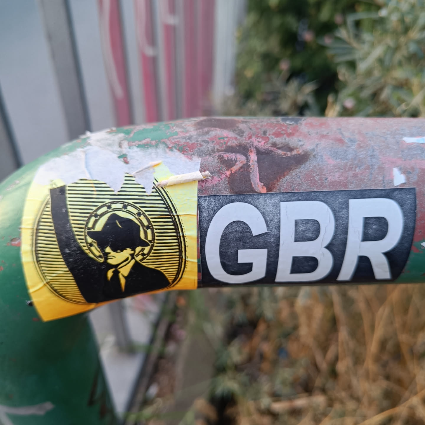 A yellow and black sticker featuring a man in a suit and hat, reminiscent of a secret agent. The text 'GBR' is visible on a separate sticker next to it.