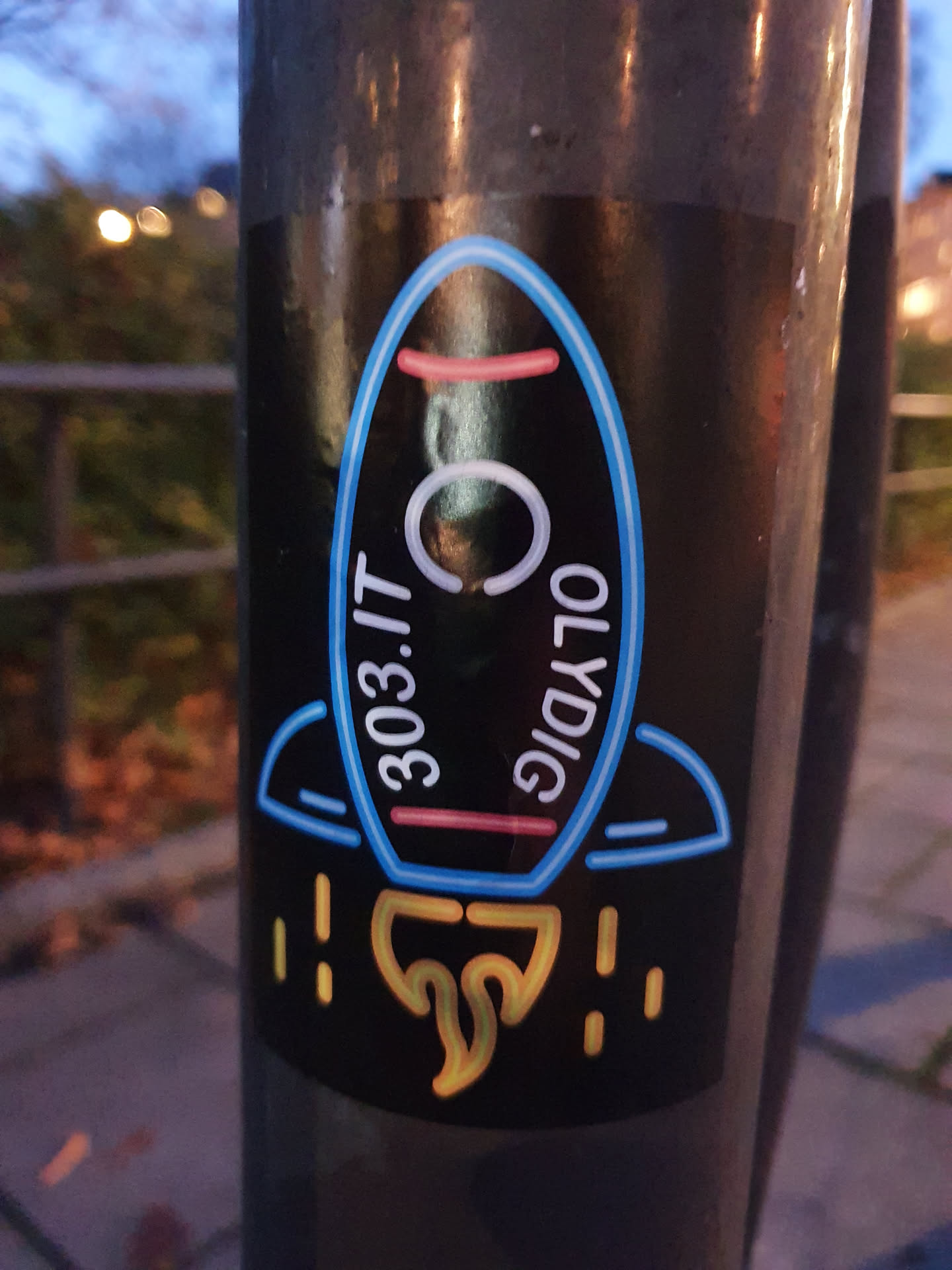 A sticker featuring a rocket with the text "303.IT" and "OLYDIG" written on it, designed with a neon effect.